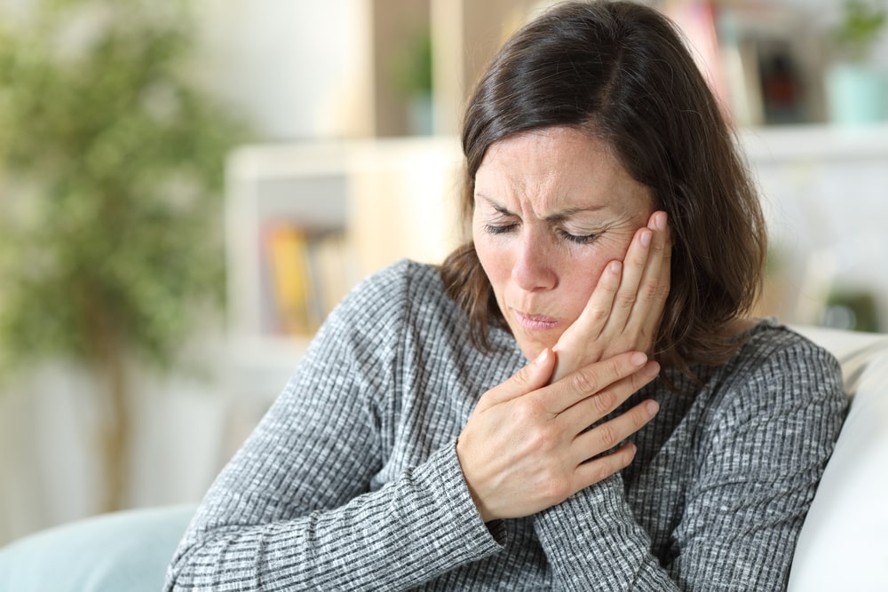 donna di mezza età si tocca la guancia e prova dolore a causa di un mal di denti dovuto a scarsa igiene orale